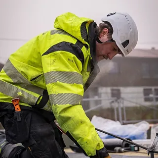 Taktekker monterer takmembran på flatt tak med verneutstyr for sikker og tett takløsning.