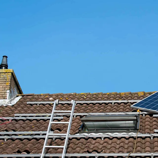 Montør installerer solcellepanel på tak med fallsikring og festesystem for trygg montering.