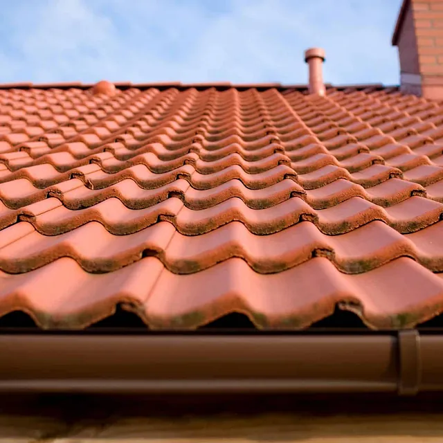 Detaljbilde av takstein med takrenne, pipe og beslag på tradisjonelt skråtak ved bolig.